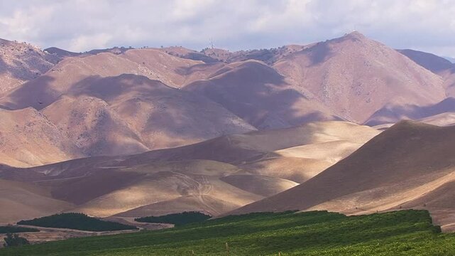 Cloud shadows drift over the grassy golden foothills of California's southern Sierra Nevada mountains near Bakersfield and the Kern River Canyon entrance.  Orange orchards carpet the foreground.