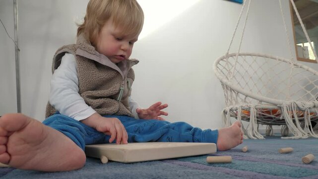 Joyful toddler plays game with wooden sticks, solitaire game. Baby enhancing creativity and fine motor skills while exploring their surroundings and fostering sense of wonder