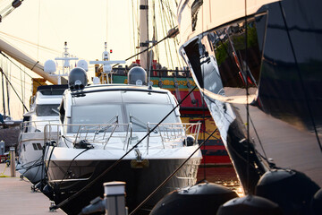 A yacht club at sunset, yachts and sailboats are moored to the berths, huge fenders hang on mega yachts, thick ropes, reflections in the glossy sides of boats, the glare of sun on water surface