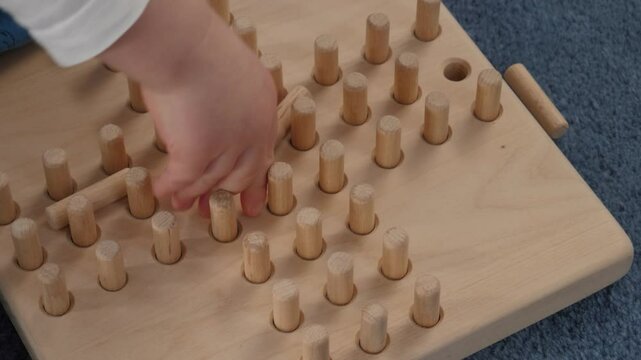 Small toddler hand plays game with wooden sticks, solitaire game. Baby enhancing creativity and fine motor skills while exploring their surroundings and fostering sense of wonder