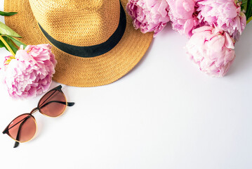 Straw hat, sunglasses and pink peonies arranged on white background, top view summer fashion concept. Flat lay, copy space