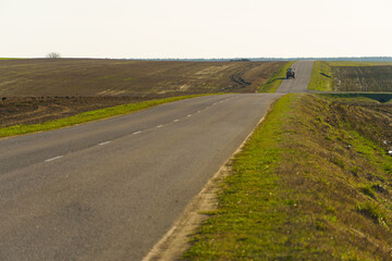 An empty asphalt road outside the city passes by a rural field and a blooming meadow. Travel by car...