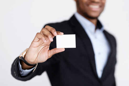 Fototapeta Business Card Mock-Up. Smiling black businessman holding blank card for clients or business partners, selective focus on empty white card, grey studio background, closeup, copy space