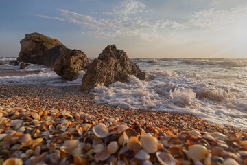 Splashing waves beat against the rocks on the beach at sunset
