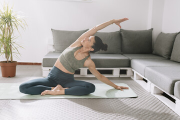 Fototapeta premium Woman practicing yoga at home on a mat in a serene living room with green plants