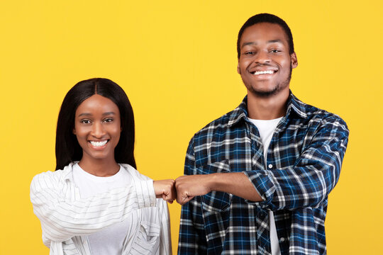 Work as team, agree to do, partnership and collaboration. Young teen happy african american couple give fist bump, agree to bring plan to life, isolated on yellow background, studio shot, free space