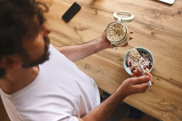 A person is preparing a nutritious breakfast at home, holding a jar of oats in one hand and a...