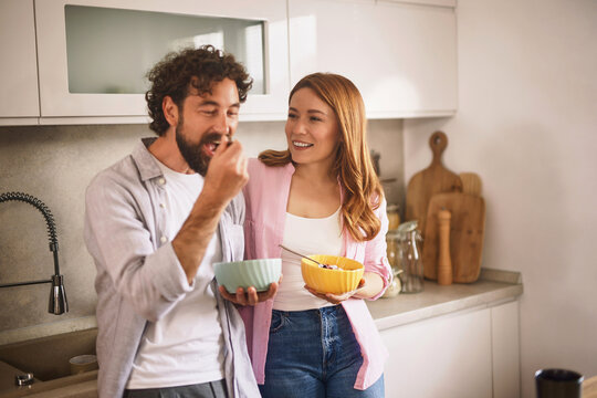 A cheerful couple shares breakfast in a stylish kitchen, engaging in conversation and smiles while enjoying their meal in a cozy atmosphere.