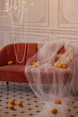Red velvet sofa draped with white tulle and lemons in classic room with ornate wall and chandelier....