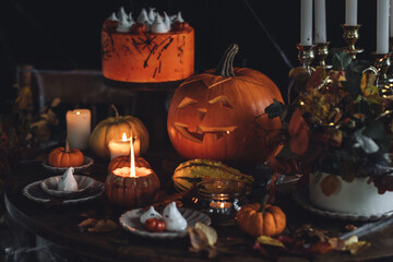 Homemade delicious chocolate cake with coloured orange cream and meringue ghosts, pumpkins for Halloween home party. Elegant beautiful table arrangement with candles, chandelier, Jack-o-Lantern 