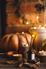 Autumn cozy mood composition with burning candles. Aroma stick reed diffuser, pumpkin on wooden table, knitted warm plaid. Fall hygge home decor, aromatherapy. Relaxed atmosphere in the apartment