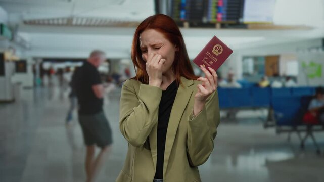 Woman holding chinese passport covers nose in busy airport terminal, indicating bad smell and uncomfortable travel situation.