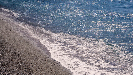 Gentle waves washing over a pebble beach on a sunny day in Scilla, Southern Italy