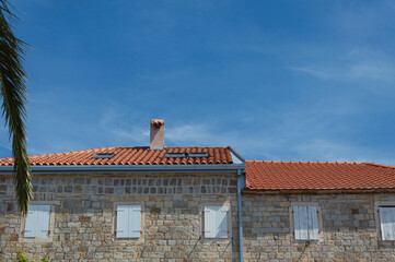 Obraz premium Old stone house with small windows, tiled roof and blue sky on the Adriatic coast in Montenegro Petrovac