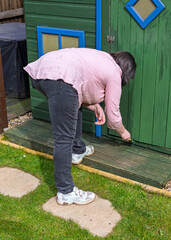 Woman bending forward to Paint Wooden Playhouse Door With Green Paint