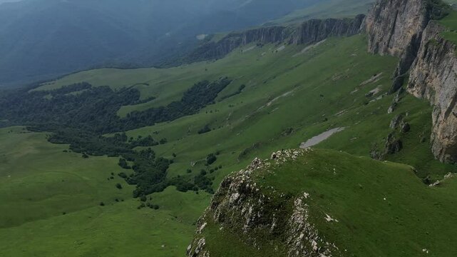 Circular drone flight around a rocky formation in green mountains. Beautiful landscape and terrain against a clear blue sky.