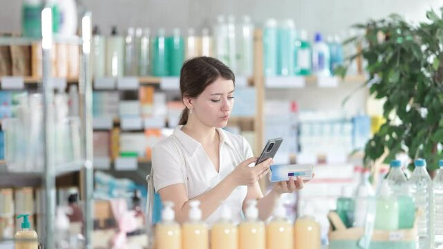  Young woman buyer scanning qr code for box of ointment in pharmacy