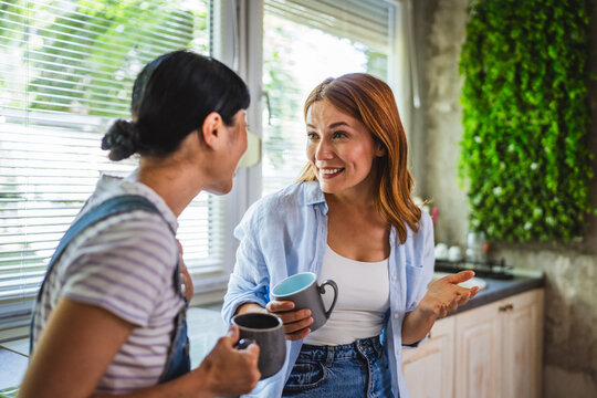 two diverse female friends talk and enjoy at kitchen while drink coffee