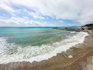 Peaceful summer beach with turquoise ocean waves, rocky pier, blue sky, and natural seascape, perfect for travel and nature themes