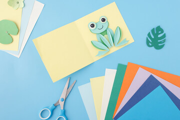Crafting scene with colored paper, glue, and scissors, top view. Ideal for stationery brand...