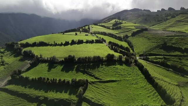 Drone hovers over rolling green hills with the sun shining through the clouds