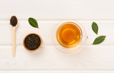 Cup of tea with dry and fresh leaves on wooden background, top view