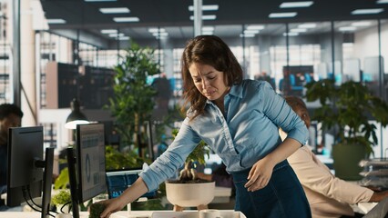 Upset worker in office packing desk plants on last day at work after quitting, saying goodbye to colleague. Employee getting fired from job during layoffs, saddening coworkers, camera A