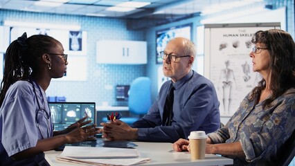African american nurse takes notes during consultation with old people, healthcare records with symptoms and other problems. Ensuring an easy recovery plan, clinical setting. Camera A.
