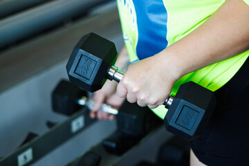 Arm view of a young, overweight Latina woman exercising with weights in a gym, pushing herself, and looking at weights. Health, improvement, and well-being.