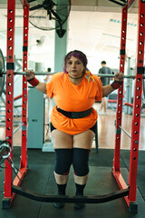 View of a beautiful, overweight young Latina lifting weights and working out at a gym. Positively, she's pushing herself to the limit. She's improving and feeling better.