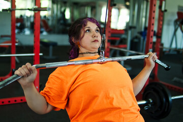 Beautiful, overweight Latina woman concentrating on lifting weights on an exercise machine at a gym. Wearing colorful clothes, hair, and retro makeup, she's positive. She's pushing herself.