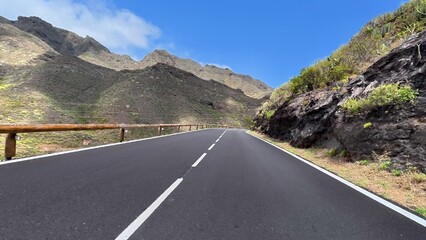 Fototapeta premium A Scenic Mountain Road Surrounded by Lush Greenery and Under a Bright Blue Sky Above