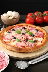 Tasty pizza, ingredients and cutter on black wooden table, closeup