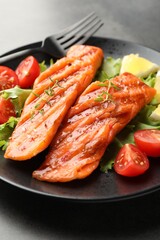 Tasty grilled salmon served with lettuce, tomatoes and lemon on grey table, closeup