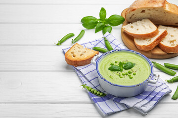 Tasty pea cream soup with basil served on white wooden table. Space for text