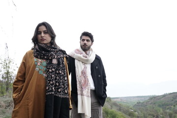 A couple posing in traditional Kashmiri attire, adorned in handwoven shawls and embroidered pherans, showcasing the rich heritage and artistry of Kaar Kash in a styled fashion shoot.

