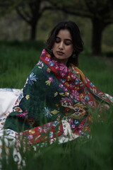 Girl wrapped in a luxurious silk carpet, seated on an intricately embroidered sheet laid over...