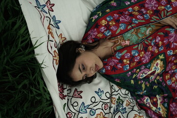 Woman lying peacefully on a traditional carpet spread over lush green grass, blending comfort,...