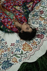 Woman lying peacefully on a traditional carpet spread over lush green grass, blending comfort,...