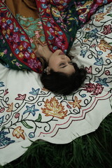 Woman lying peacefully on a traditional carpet spread over lush green grass, blending comfort,...