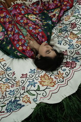 Woman lying peacefully on a traditional carpet spread over lush green grass, blending comfort,...