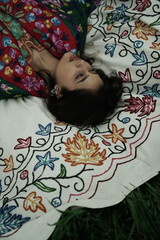 Woman lying peacefully on a traditional carpet spread over lush green grass, blending comfort,...