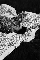 Woman lying peacefully on a traditional carpet spread over lush green grass, blending comfort,...