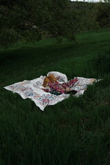 Woman lying peacefully on a traditional carpet spread over lush green grass, blending comfort,...