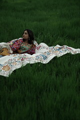 Woman lying peacefully on a traditional carpet spread over lush green grass, blending comfort,...