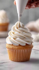 
A young baker pipes elegant white buttercream onto a cupcake. The swirl forms gracefully under natural light on a white kitchen counter.  
