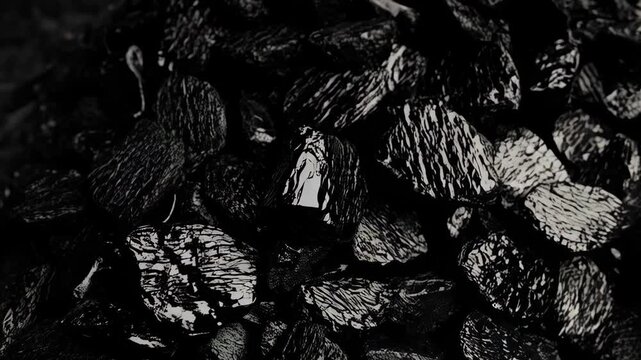 Pile of raw, rough black coal in a dark, shadowy environment used for fuel or industry. Texture of fossil fuel creates an abstract dark and light contrast.