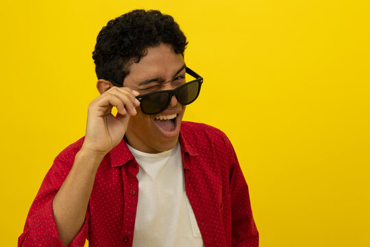Close up of cheerful young Latino man in red casual clothes taking off his glasses while making winking expression