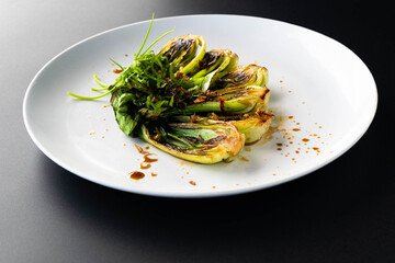 Grilled bok choy garnished with fresh herbs and drizzled with sauce on a sleek black background.