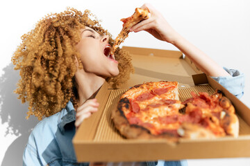 A joyful young woman enthusiastically enjoying pizza from a delivery box, showcasing a fun and vibrant atmosphere with her curly hair and casual outfit